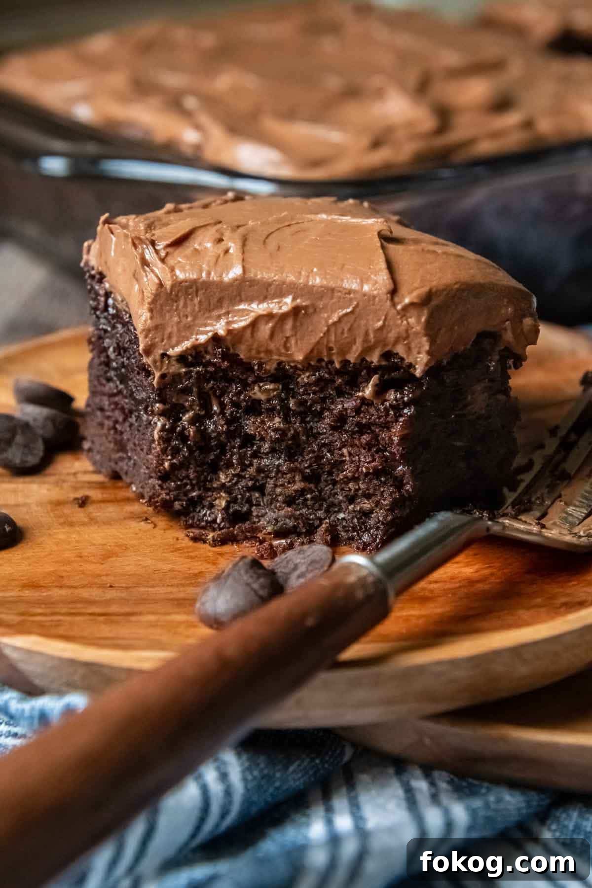 a slice of chocolate cake on a wood plate with a bite taken out
