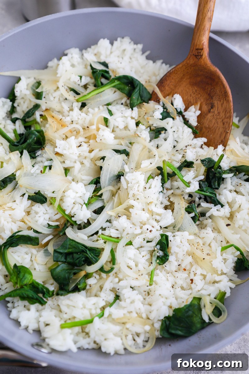 A large skillet filled with white rice sauteed with white onions and spinach