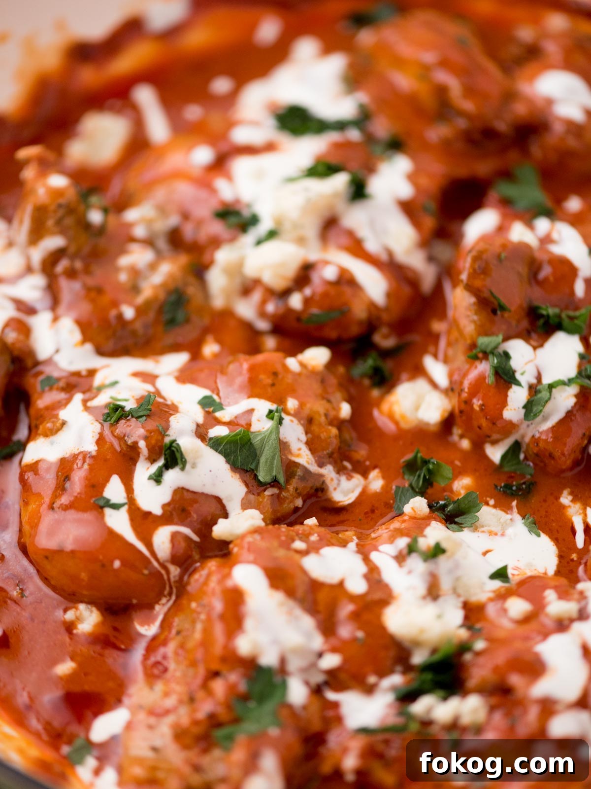 Crispy Buffalo Chicken Thighs Recipe for Dinner 7 buffalo chicken thighs in a skillet surrounded by fresh parsley, a serving utensil, and a kitchen towel