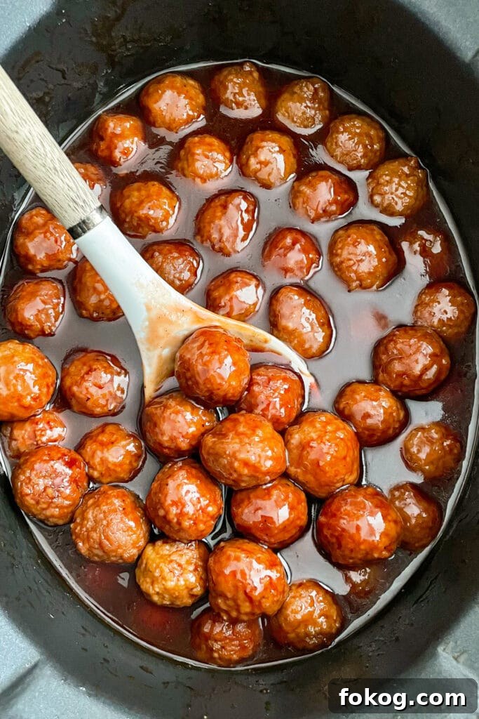 grape jelly meatballs in the slow cooker with a serving spoon