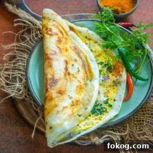 Crispy Egg Dosa (Mutta Dosa) Recipe for Perfect Breakfast 16 A crispy Egg Dosa served on a green plate with red chilies, cilantro, and a small bowl of podi on the side.