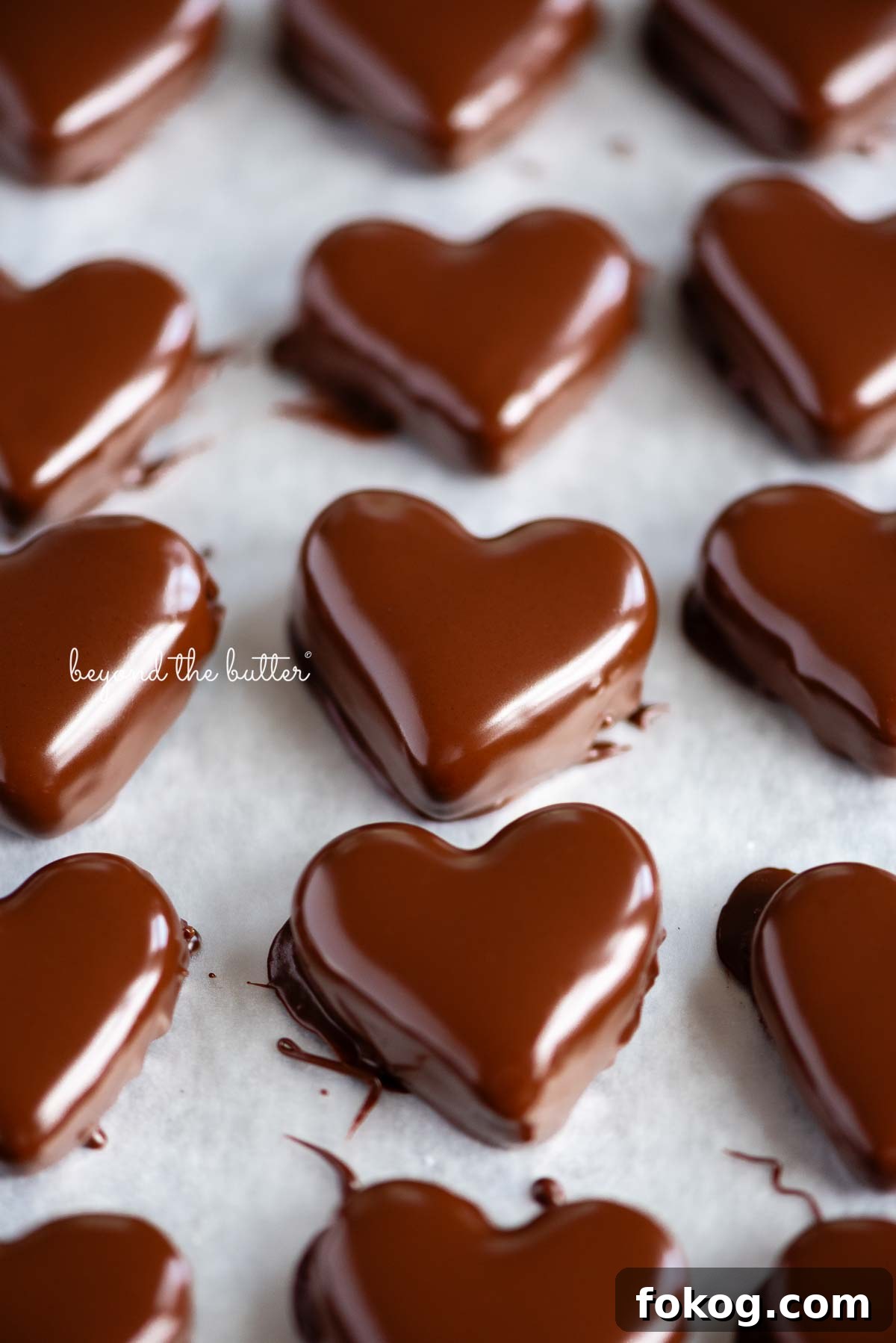 Rows of just dipped chocolate covered peanut butter hearts on a wax paper lined baking sheets.
