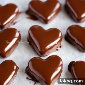 Rows of just dipped chocolate covered peanut butter hearts on a wax paper lined baking sheets.