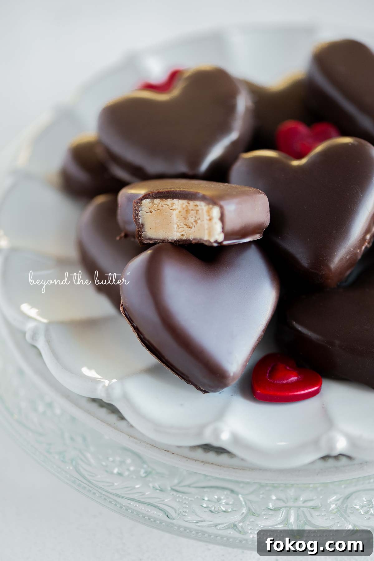 Chocolate covered peanut butter hearts on a white ceramic dessert plate on white background with bite taken out of center peanut butter heart.