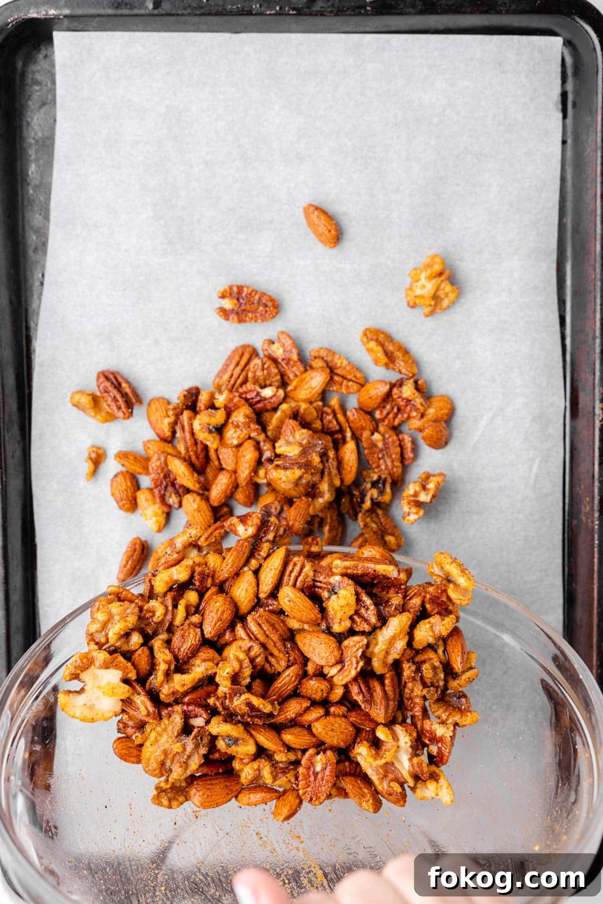 overhead photo showing spicy nut mix being poured onto a parchment-lined baking sheet