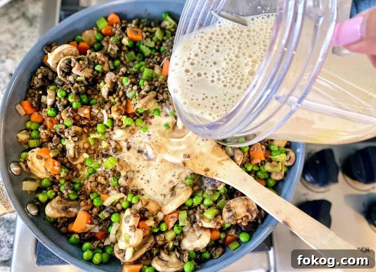 Hearty Vegan Shepherd's Pie Recipe for Comforting Weeknight Dinner 6 I am pouring the plant milk mixture into the cooking cottage pie, lentil, and vegetable mixture.