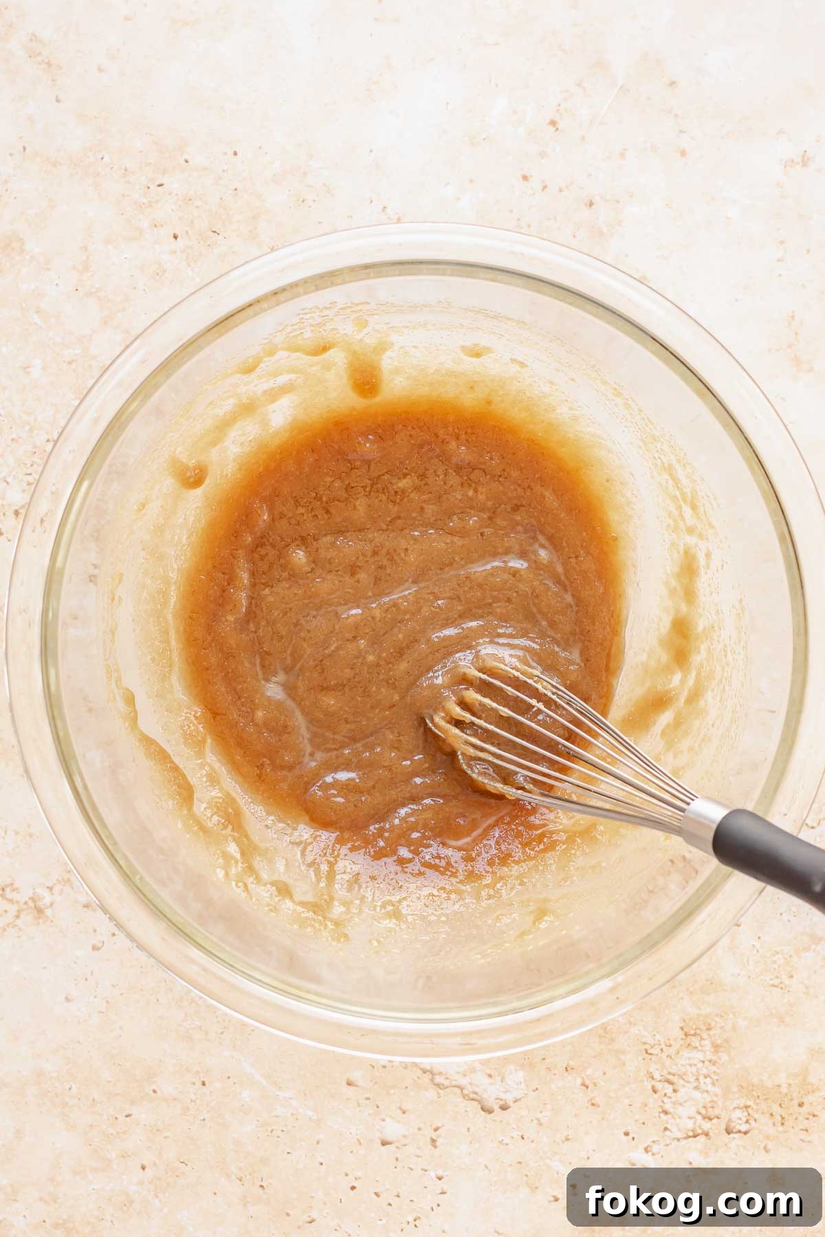A whisk mixes brown sugar and butter in a bowl.