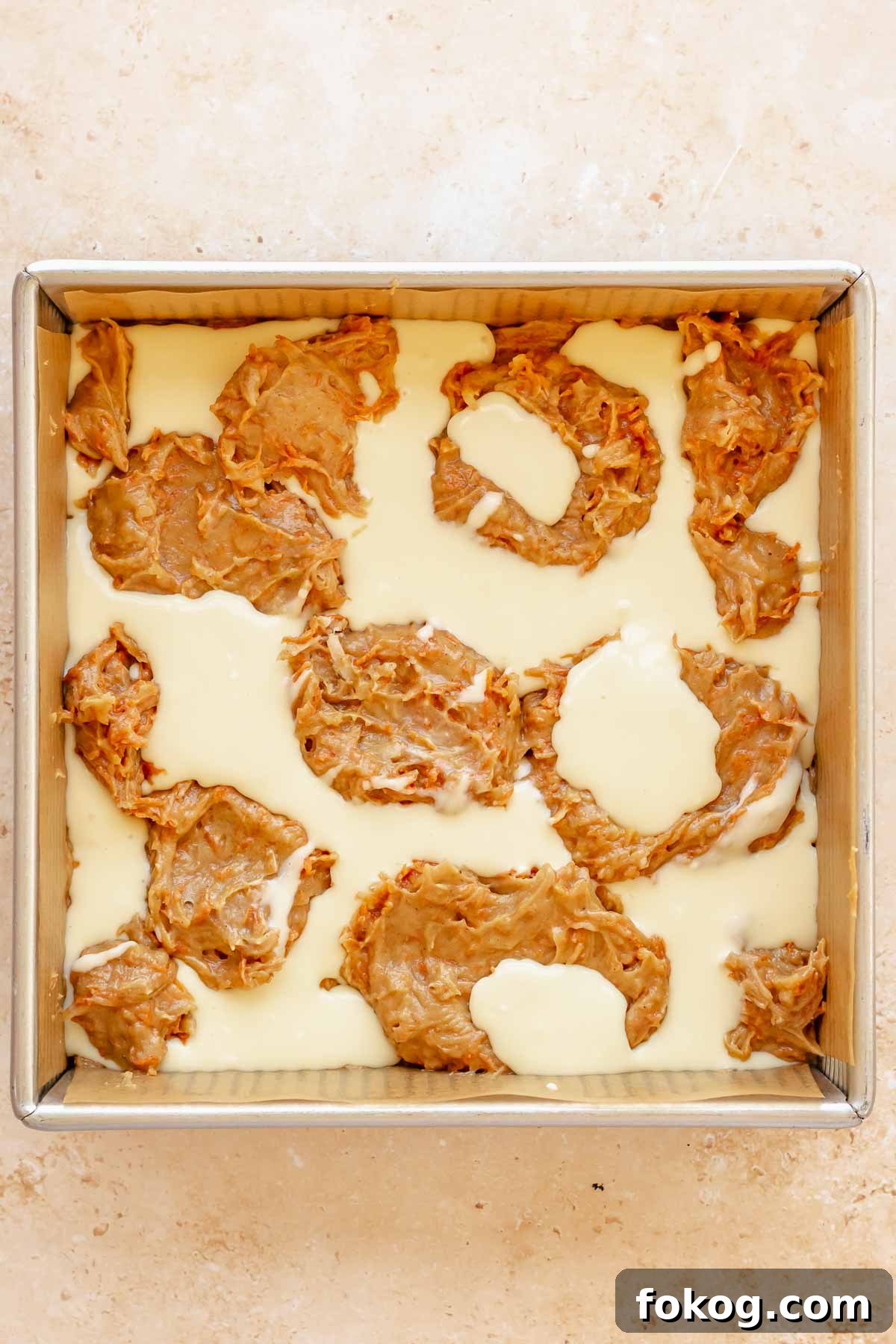Dollops of carrot cake batter and cream cheese batter alternated in a pan.