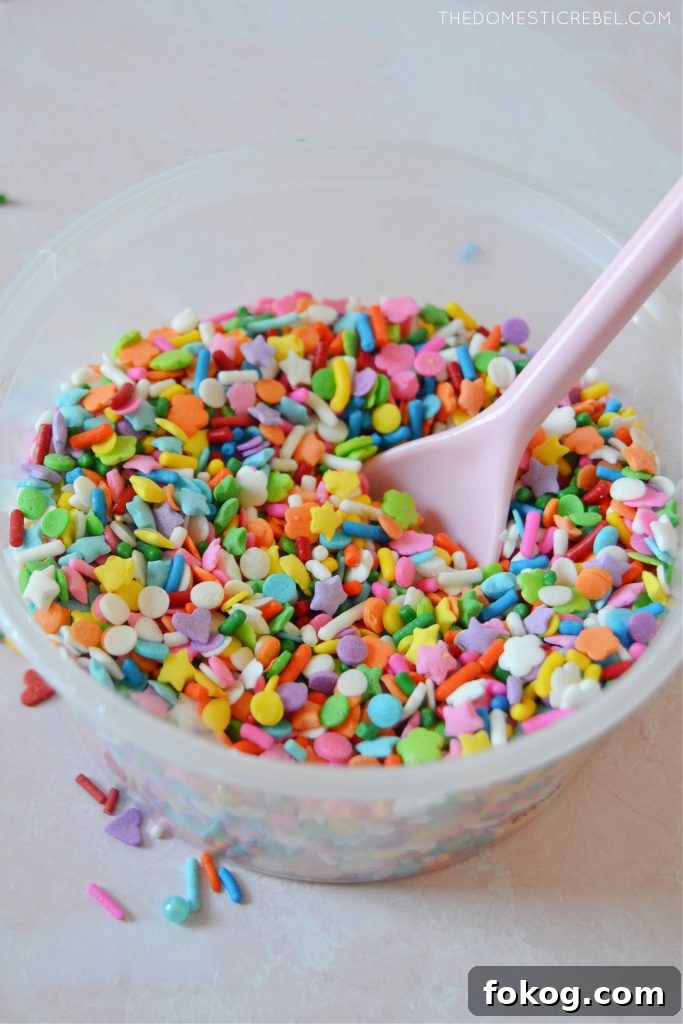bowl of rainbow sprinkle blend with pink spoon inside 