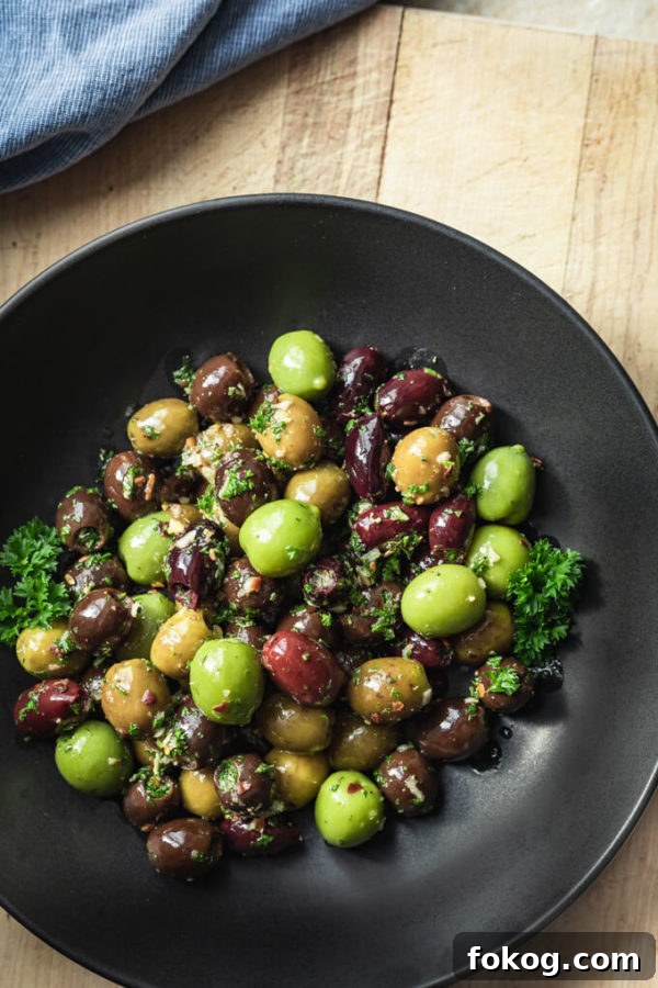 Green and black marinated olives with herbs, spices, garlic, oil and vinegar with parsley in a black bowl