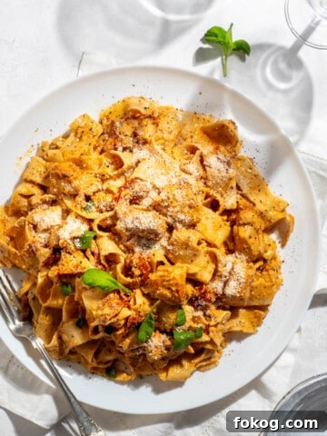 Marry me chicken pasta on a large white plate with two wine glasses.