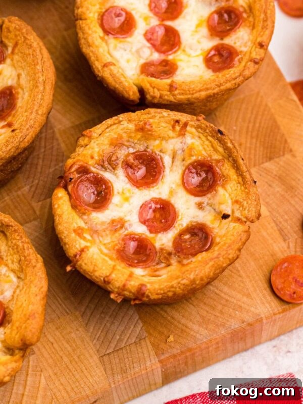 Sweet Grape Jelly Meatballs with Tangy Glaze Recipe 11 Golden crusted pizza cupcakes on a wooden cutting board with pepperoni scattered around the table.