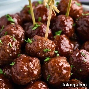 Sweet Grape Jelly Meatballs with Tangy Glaze Recipe 13 Grape jelly meatballs stacked with some skewered, in front of a slow cooker and jar of grape jelly.