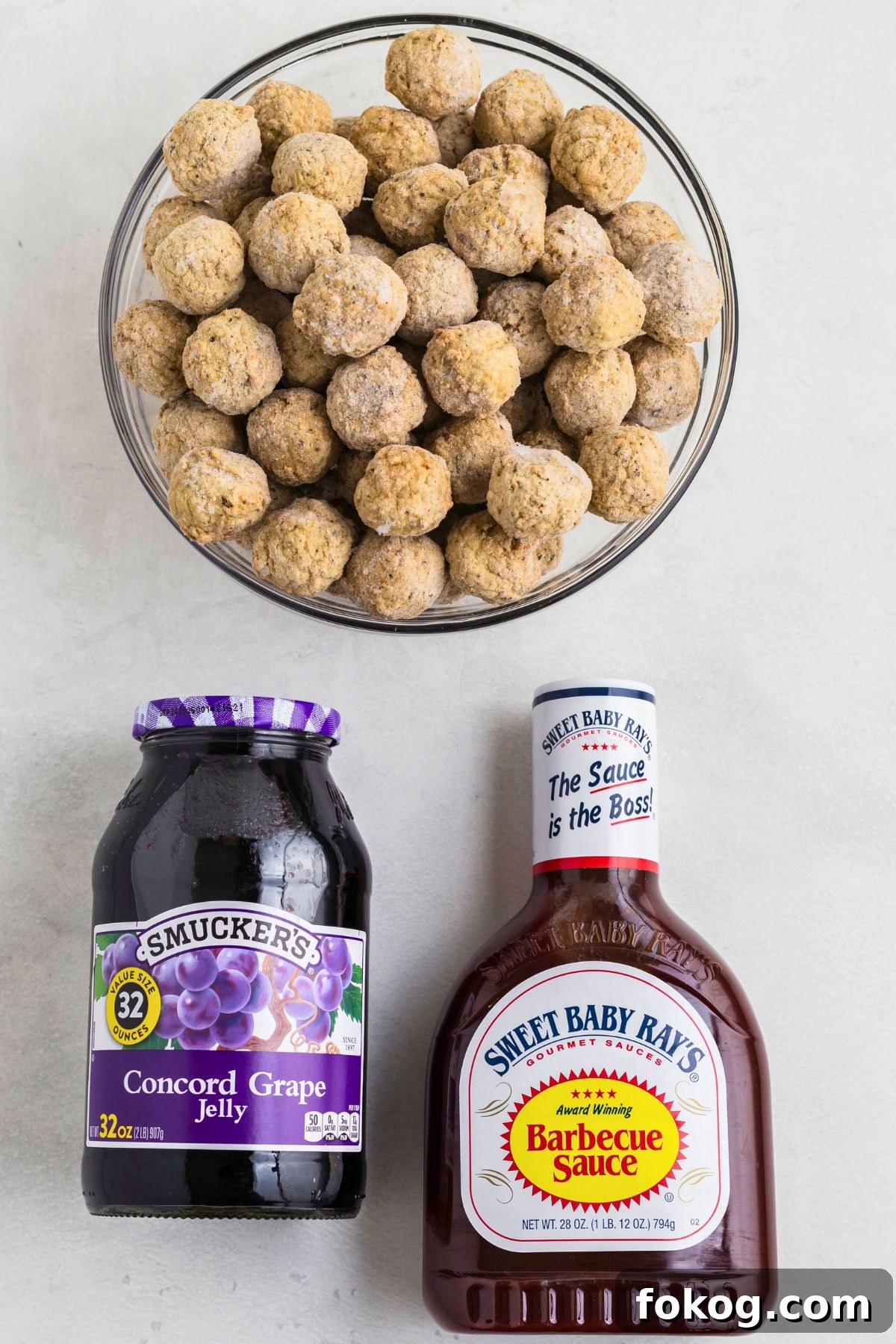 Sweet Grape Jelly Meatballs with Tangy Glaze Recipe 3 Frozen meatballs, grape jelly, and BBQ sauce, on a white marble table before mixing together in a crock pot and cooking.