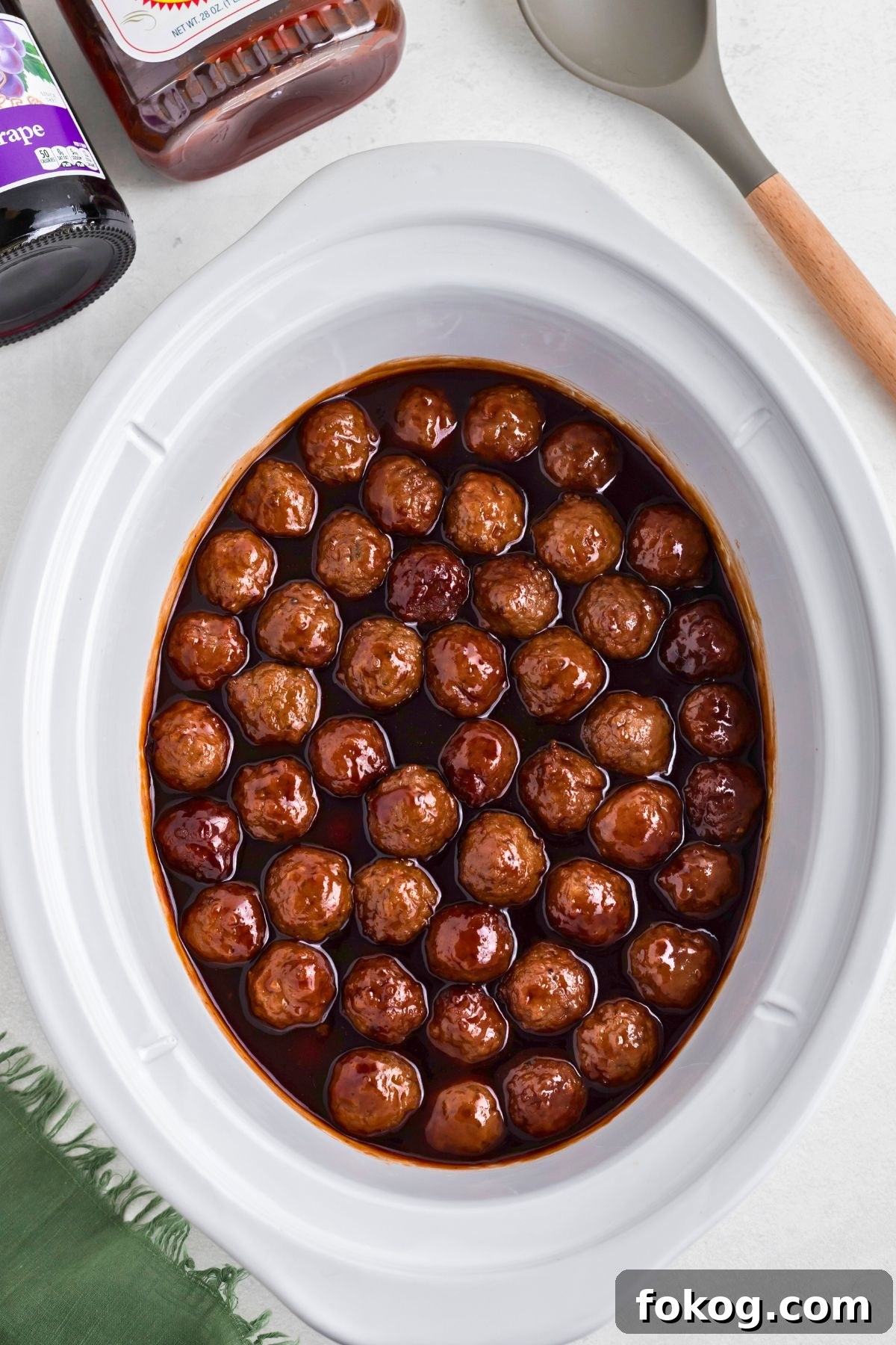 Sweet Grape Jelly Meatballs with Tangy Glaze Recipe 6 Grape jelly meatballs in a white slow cooker after cooking for 3-4 hours.