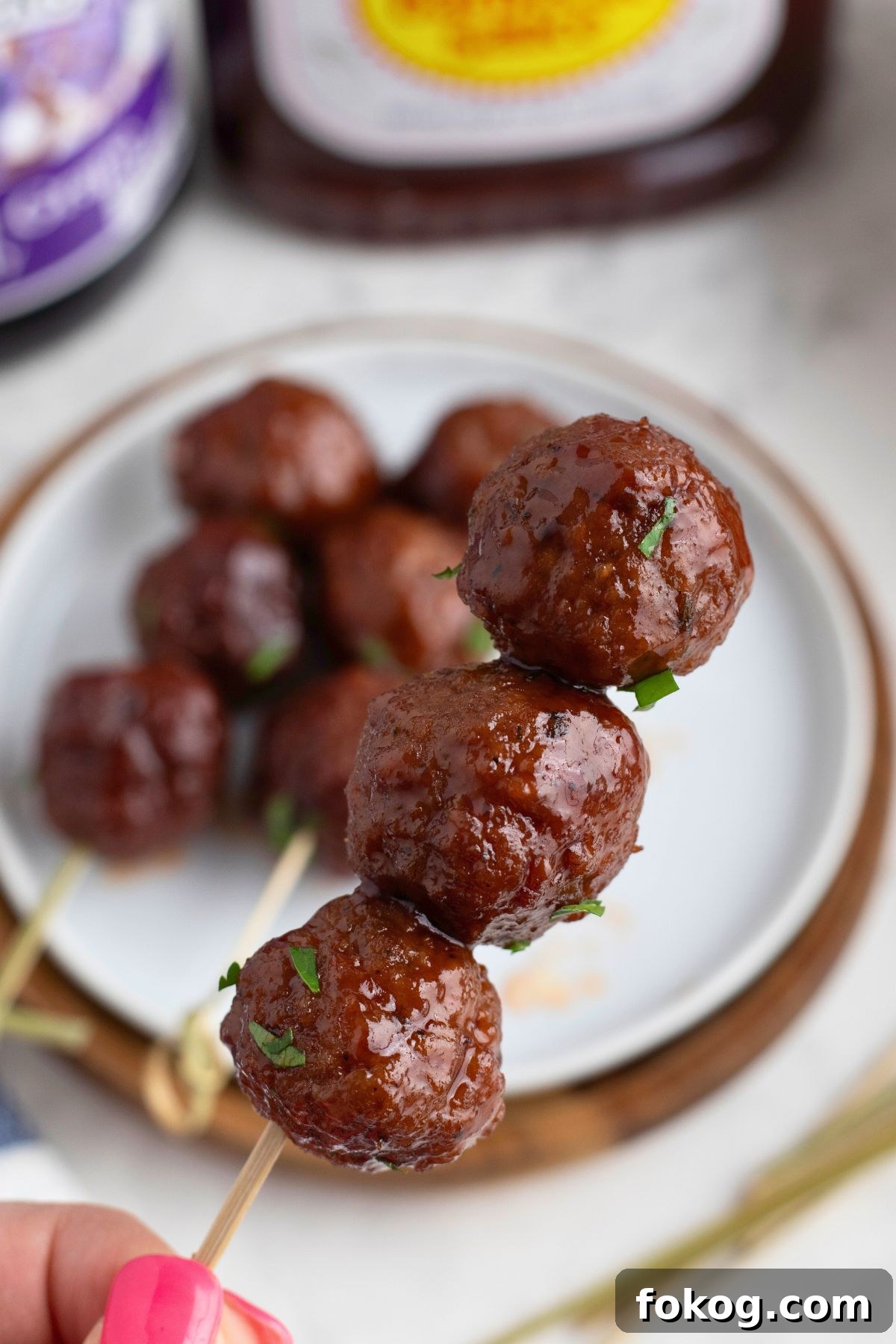 Sweet Grape Jelly Meatballs with Tangy Glaze Recipe 8 Three meatballs on a skewer over a small white appetizer plate.