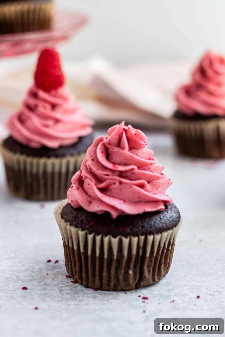 chocolate cupcakes with raspberry buttercream and a pink glass cake stand in the back