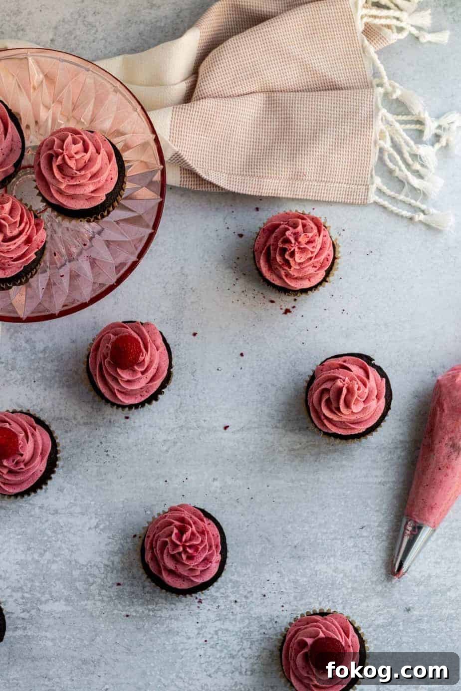 overhead view of chocolate raspberry cupcakes on a table with a piping bag of raspberry buttercream