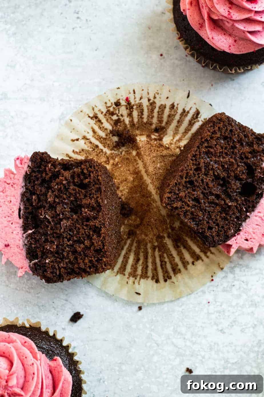 chocolate raspberry cupcake cut in half lying on a paper wrapper
