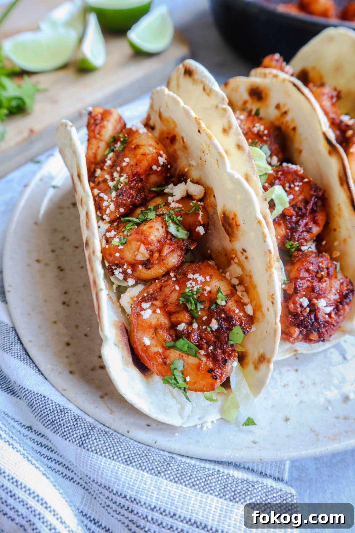 three tacos de cameron on a plate topped with cotija cheese and lettuce with limes in the background