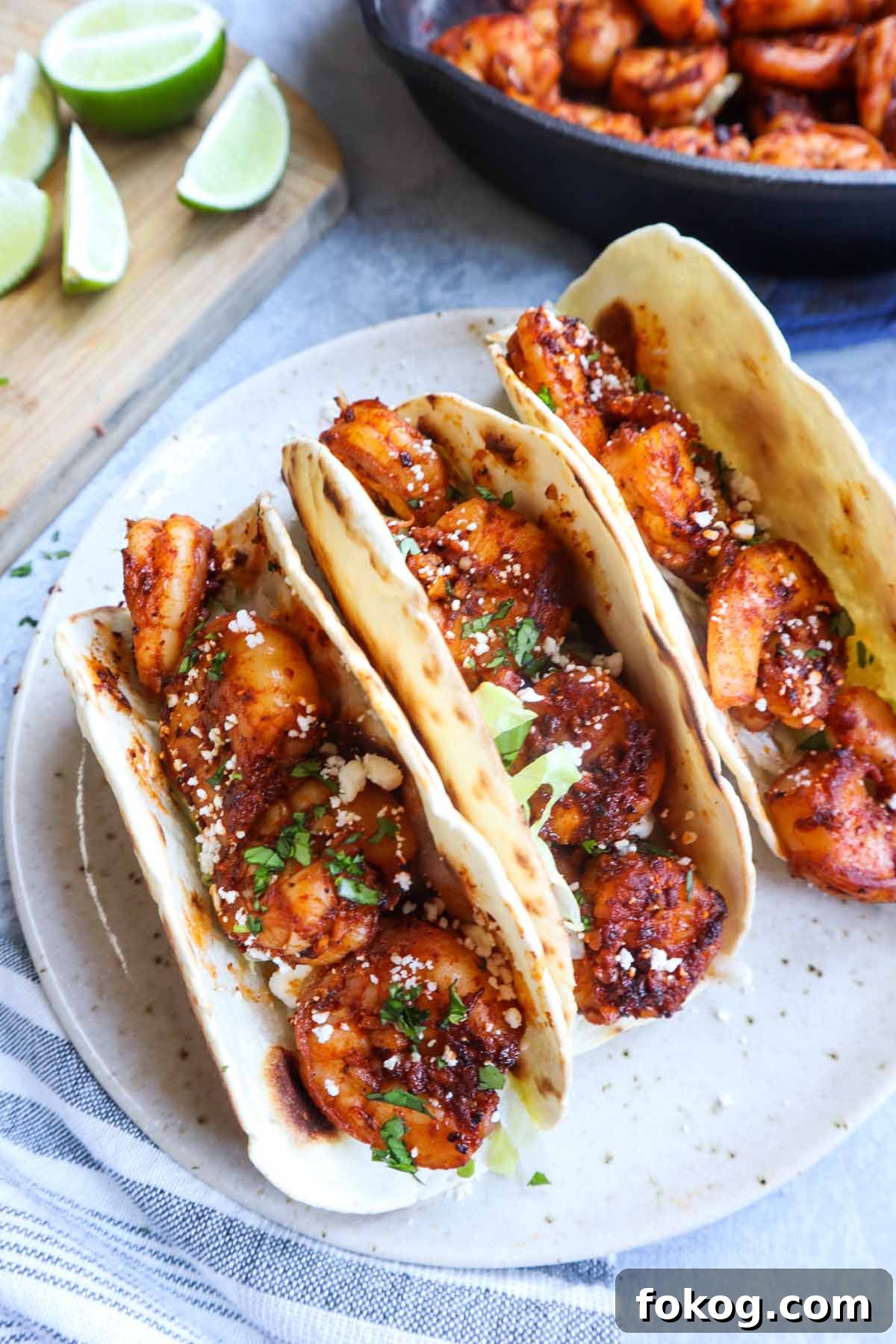 three tacos de cameron on a plate topped with cotija cheese and lettuce with limes in the background
