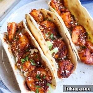 three tacos de cameron on a plate topped with cotija cheese and lettuce with limes in the background