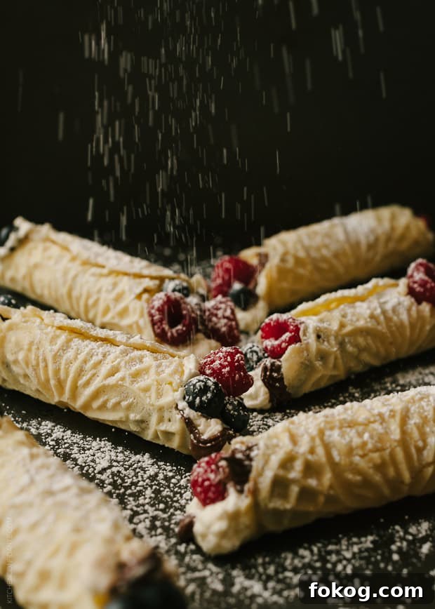 Nutella and Berry-Filled Pizzelle Waffle Cookies 6 Rolled and filled Pizzelle cookies being sprinkled with powdered sugar.