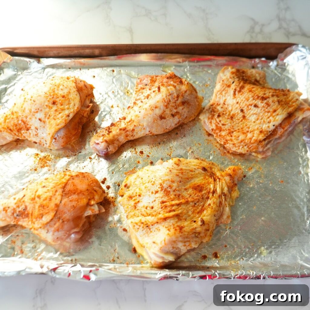 Raw chicken on a baking sheet with seasoning.