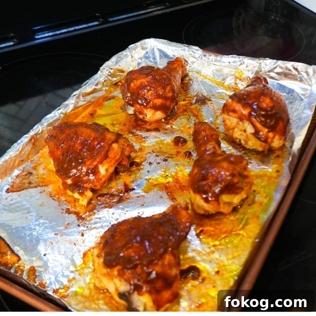Baked BBQ chicken, glazed with barbecue sauce on a baking sheet.