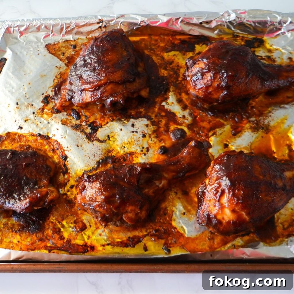 Baked BBQ chicken, glazed with barbecue sauce on a baking sheet.