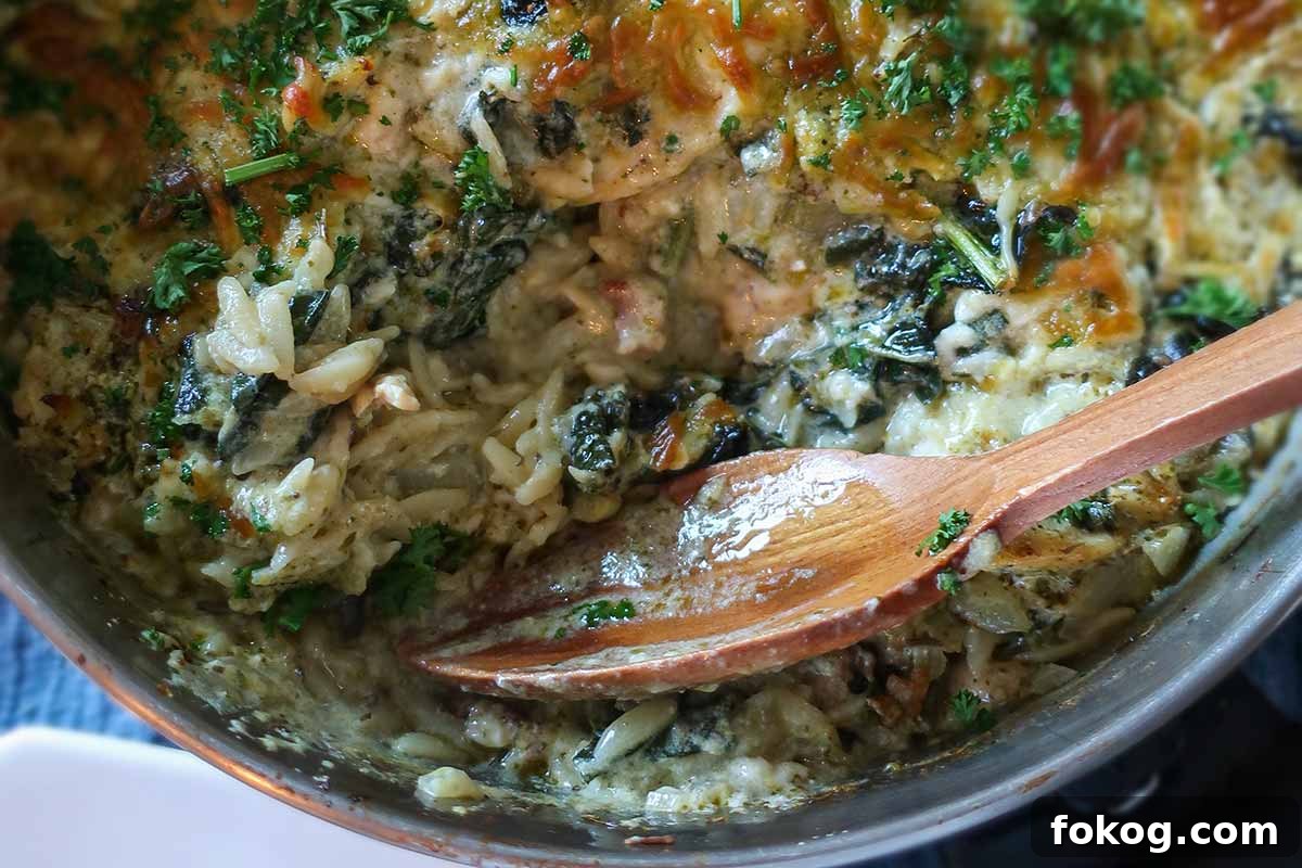 gluten free one skillet creamy pesto chicken orzo in a casserole dish with a wooden spoon