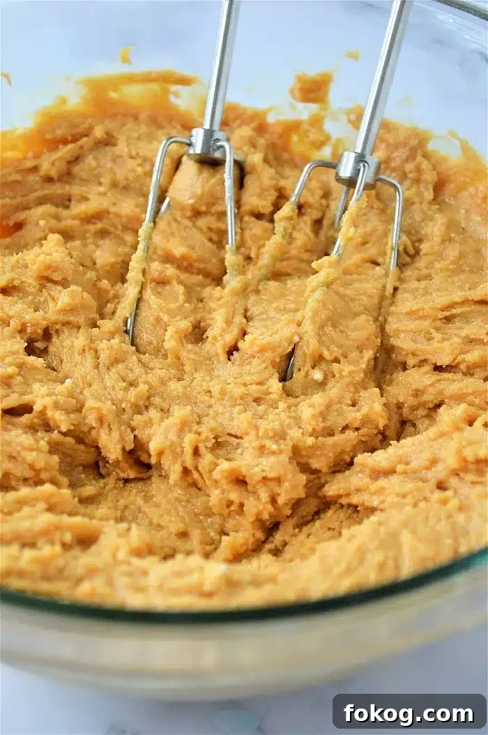 Electric beaters mixing thick cookies made with cake mix dough in a clear glass bowl.