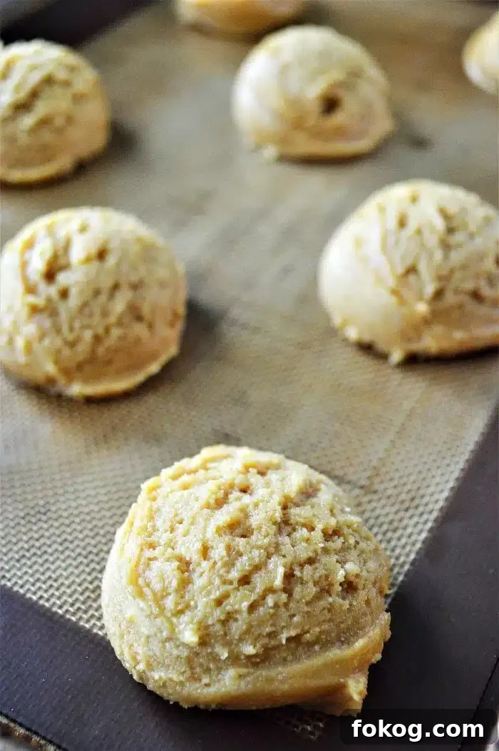 Scoops of raw cookies made with cake mix are spaced out on a baking sheet lined with a silicone baking mat.