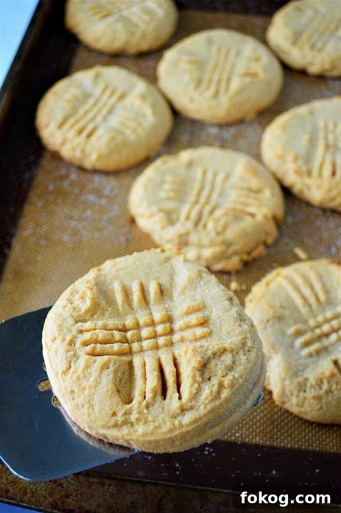 A metal spatula lifts a peanut butter cookie with a crisscross fork pattern from a baking tray, showcasing cookies made with cake mix for an extra soft texture.