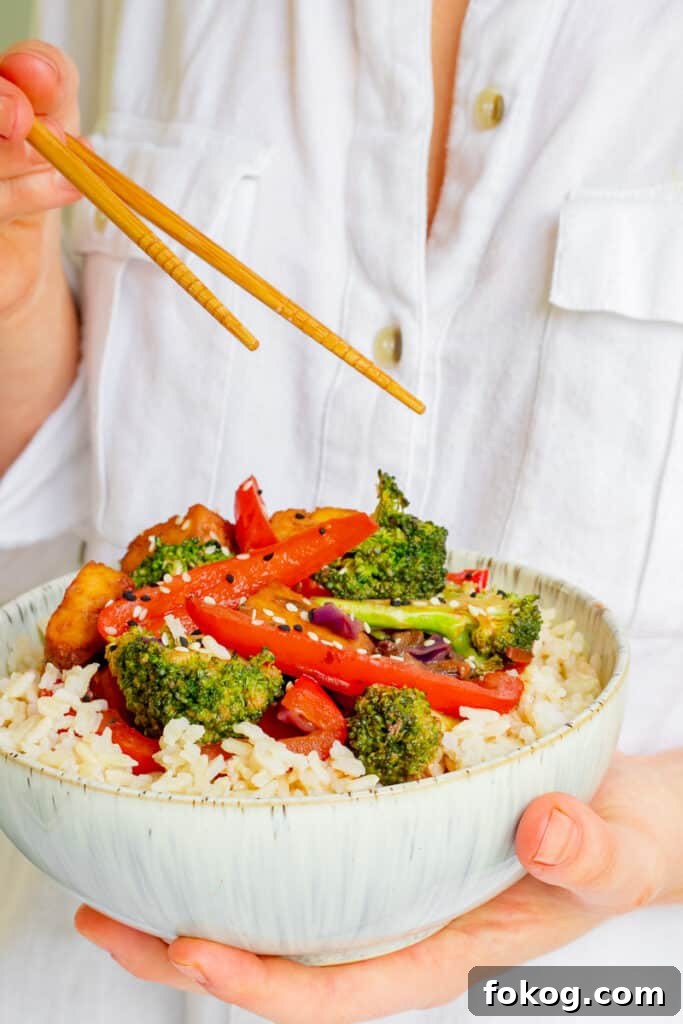Woman holding bowl of Crispy Tofu Hoisin Stir-fry. Vegan, GF & Healthy! Georgie Eats.