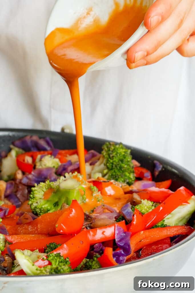 Pouring Hoisin sauce into stir-fry pan filled with vegetables.