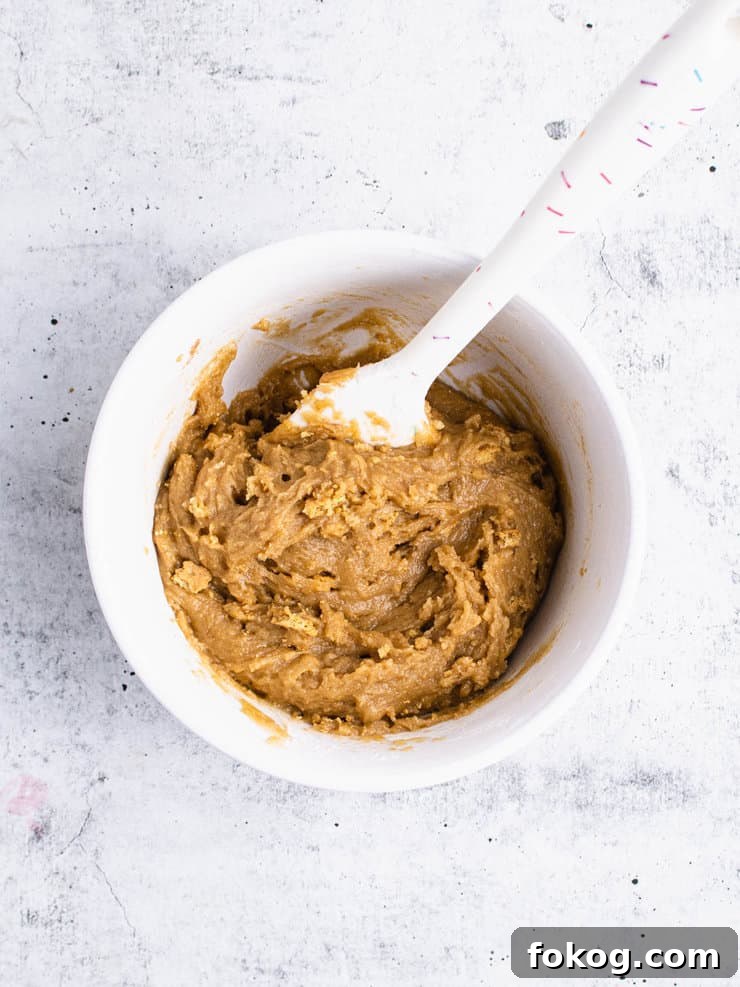 Graham cracker cookie batter in a white bowl with a white spatula sticking out of it.