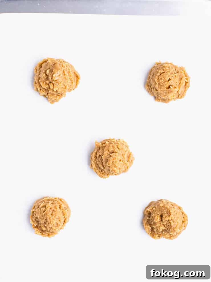 Five balls of graham cracker cookie dough on a parchment paper lined baking sheet.
