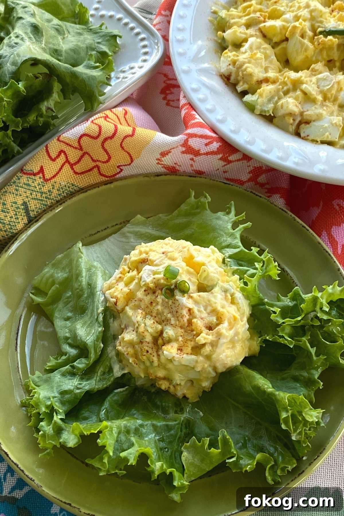 Creamy Low-Carb Keto Egg Salad Recipe for Quick Meals 6 Scoop of low-carb egg salad on a large lettuce leaf with serving bowl and more leaves behind it.