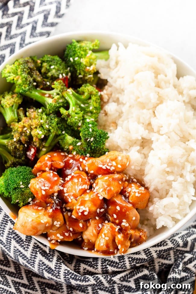 Chicken Teriyaki Rice Bowl sprinkled with sesame seeds in a white bowl with a black and cream colored napkin next to it.