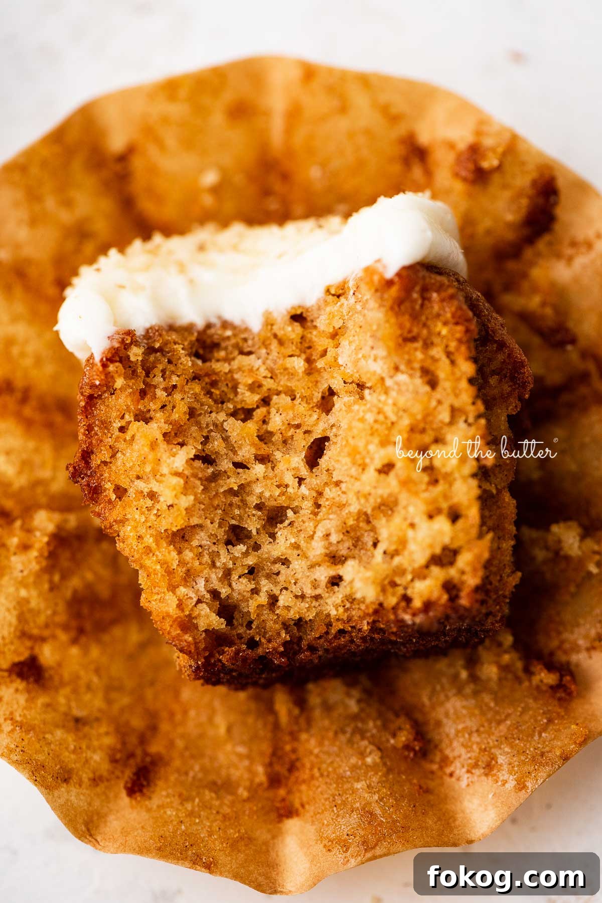 One unwrapped carrot cake cupcake with a bit taken out of it laying on its side.