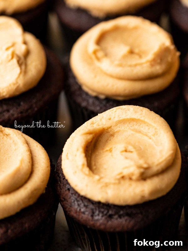 Close up image of devil's food cupcakes topped with peanut butter frosting on a baking sheet.