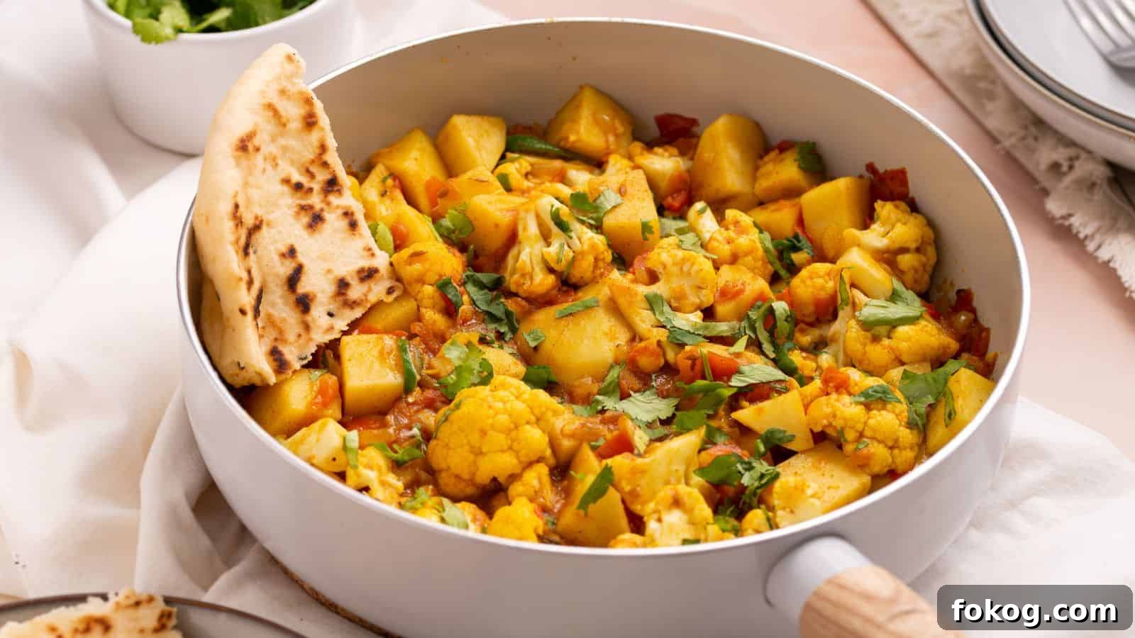 12 Irresistible Potato Recipes You’ll Love Making Again 2 A pot of vegetable curry with cauliflower and potatoes, garnished with herbs, served with naan bread.