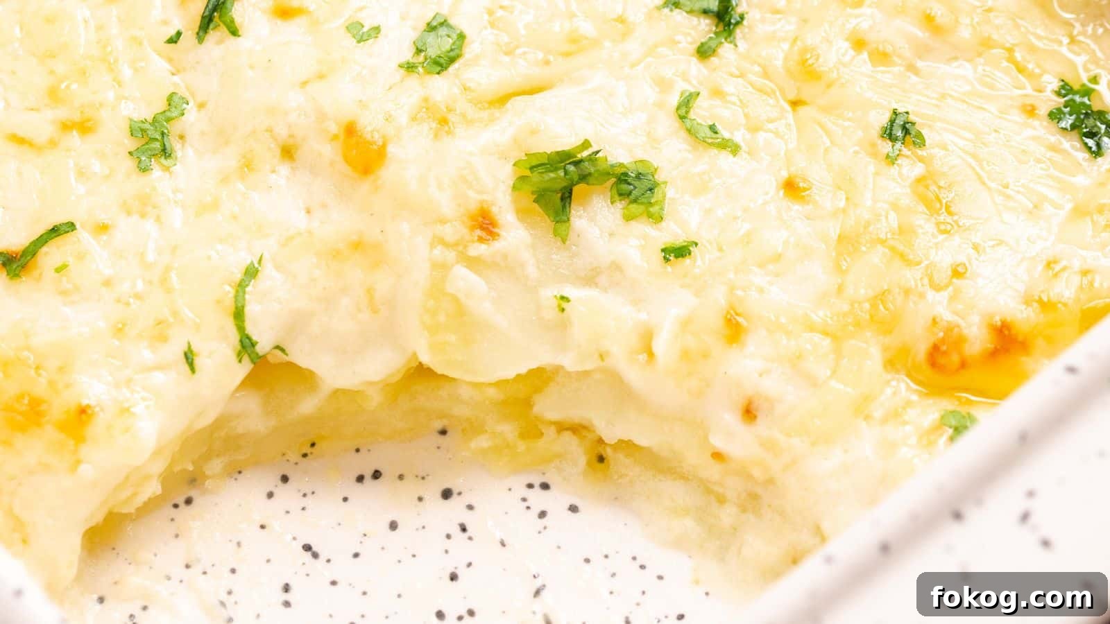 12 Irresistible Potato Recipes You’ll Love Making Again 12 Close-up of a cheesy scalloped potatoes dish in a white baking dish, garnished with parsley.