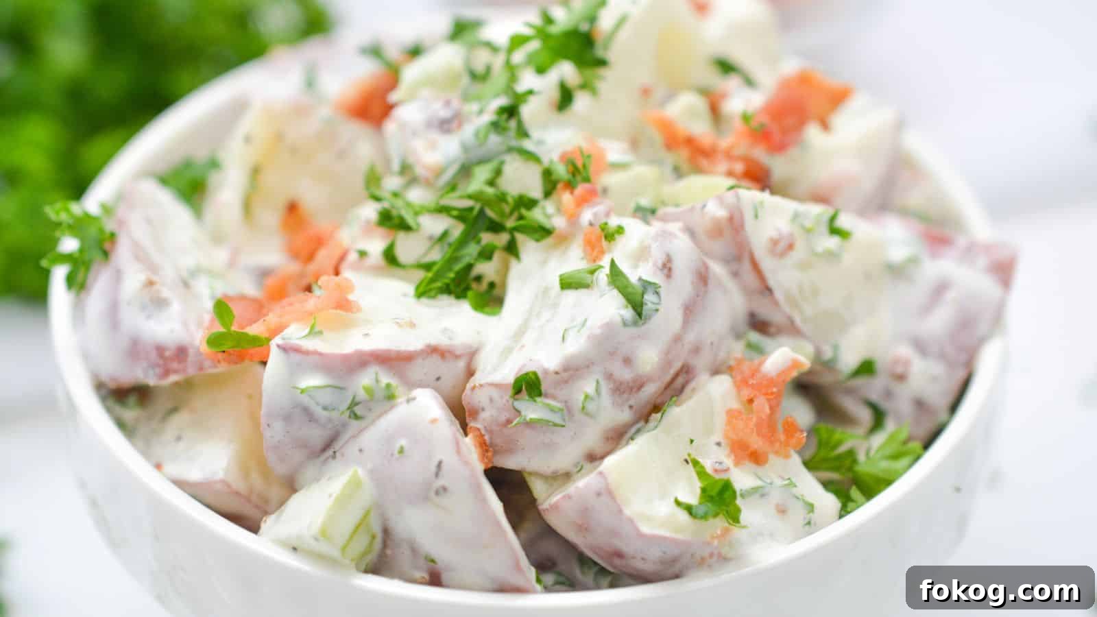 12 Irresistible Potato Recipes You’ll Love Making Again 3 Bowl of potato salad garnished with fresh herbs and bacon on a white background.