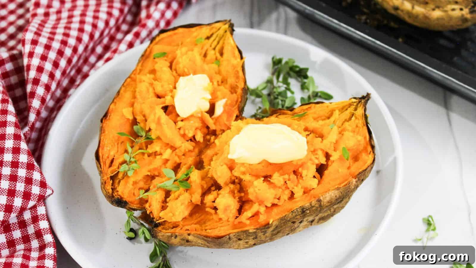12 Irresistible Potato Recipes You’ll Love Making Again 6 Two halves of baked sweet potato topped with butter and garnished with herbs on a white plate, with a red checkered napkin on the side.