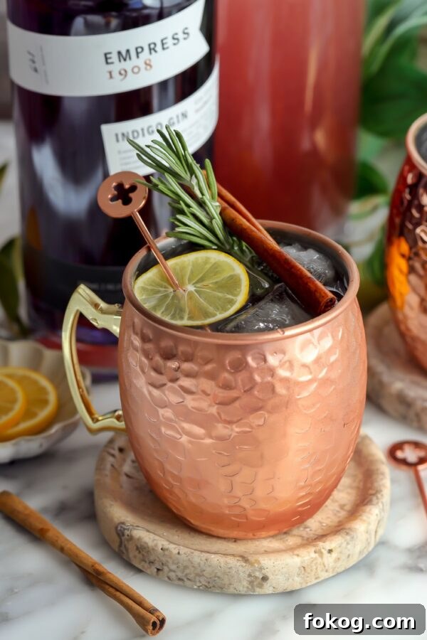This London Mule is nice a fizzy in a copper cup and garnished with a slice of lemon, rosemary and a cinnamon stick with Impress Gin in the background.