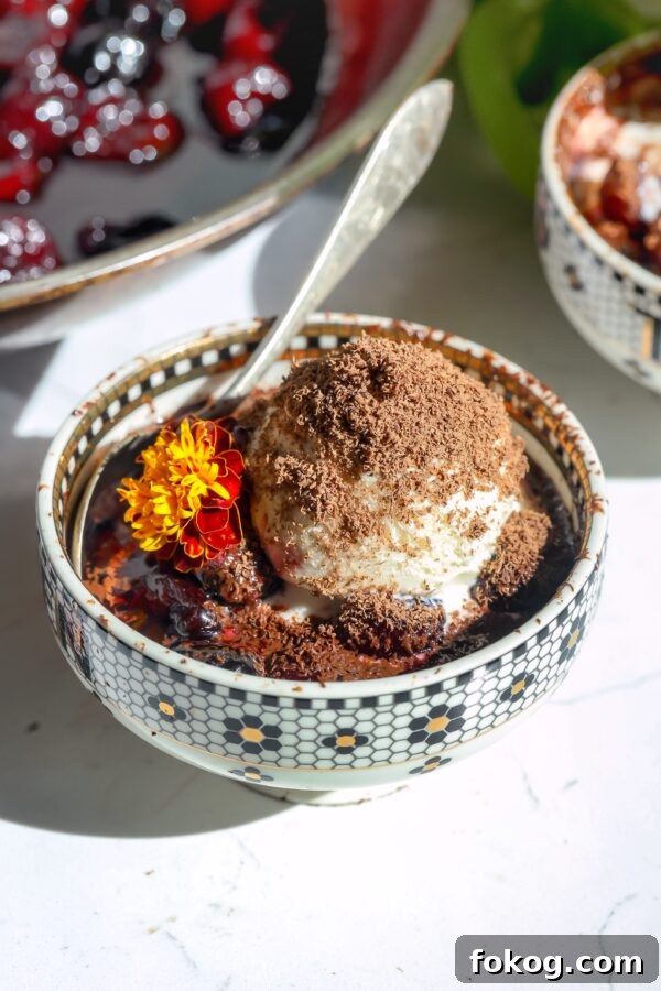 cherries jubilee with ice cream topping and shaved chocolate shavings in a bowl with a spoon.