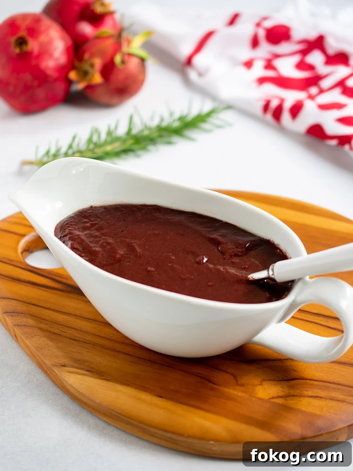 Pomegranate-Port Gravy with Rosemary for Roasts and Poultry 2 Pomegranate gravy in a white gravy boat with a white handled spoon with pomegranates in the background.