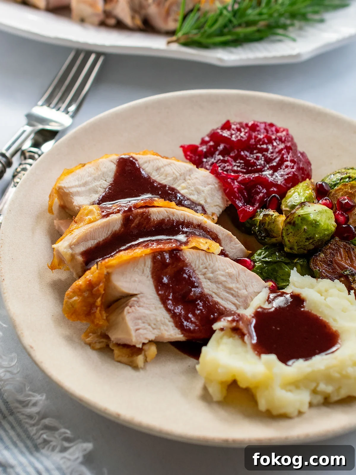 Pomegranate-Port Gravy with Rosemary for Roasts and Poultry 13 Plate of Thanksgiving food including dry brine turkey breast with pomegranate gravy and a platter of turkey in the background.